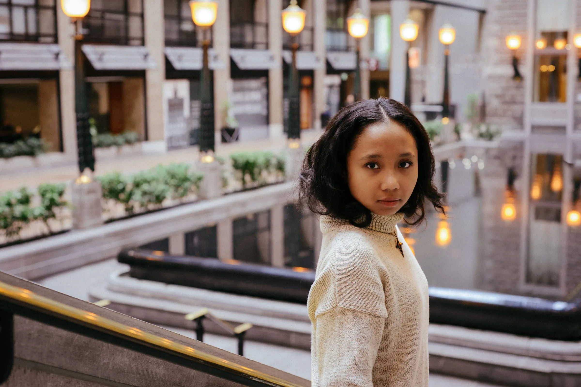 A young woman looking back over her shoulder beside a reflecting pool lined with lamps