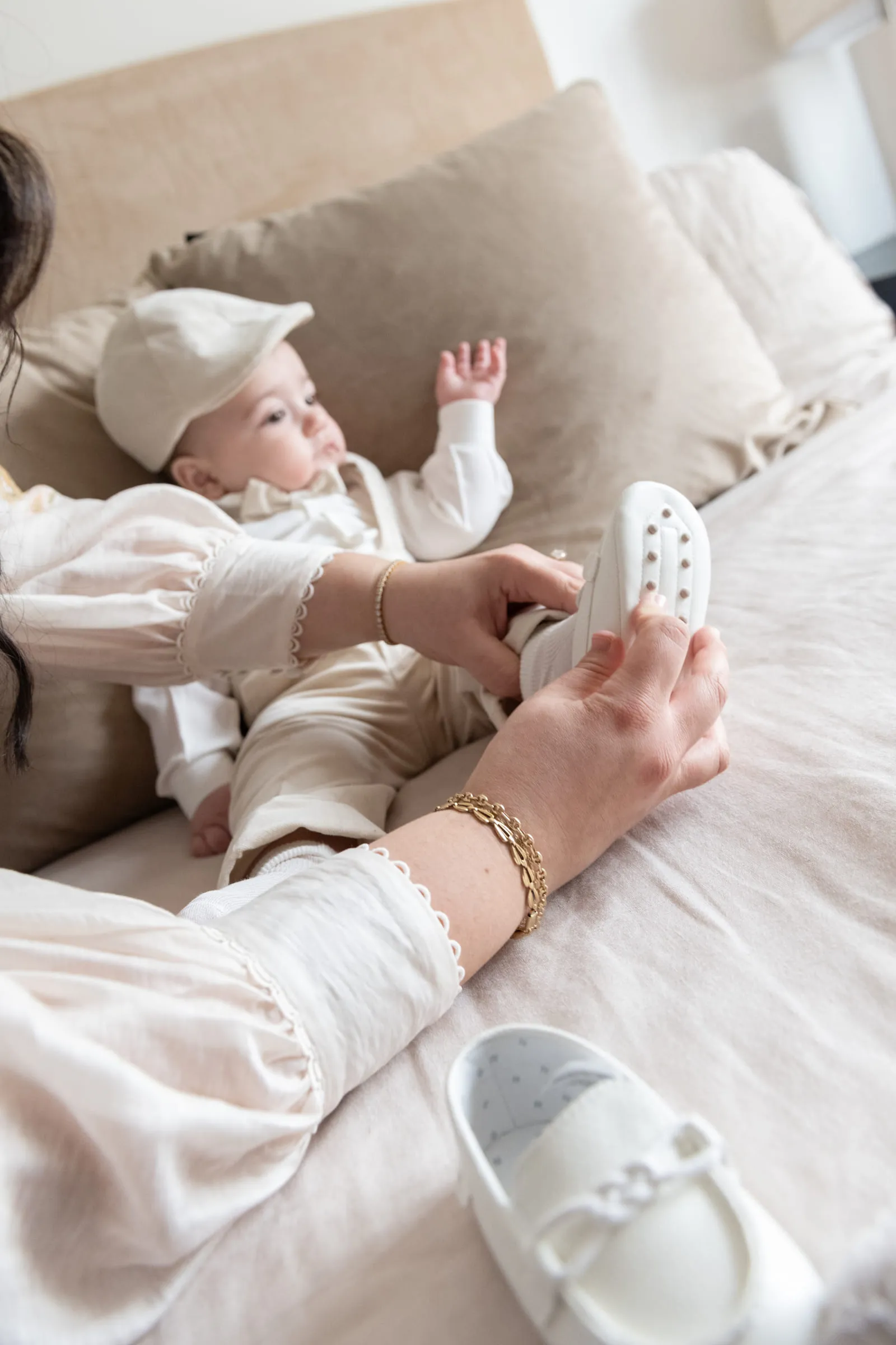 A hand easing a tiny white shoe onto the baby’s foot