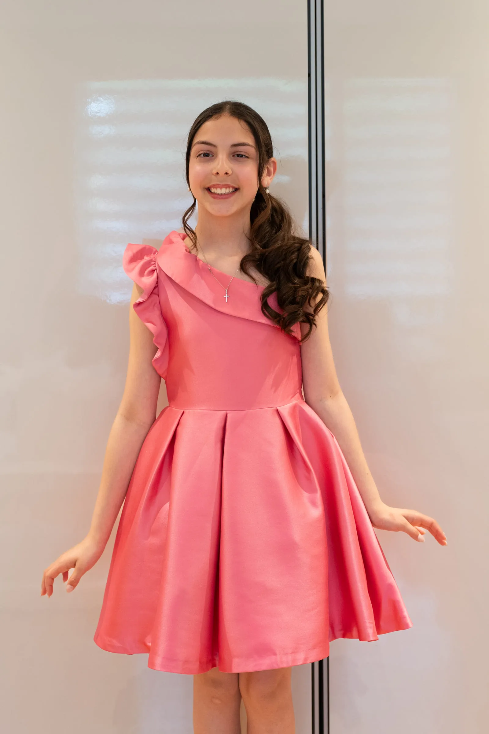 A girl in a coral dress standing against a white wall