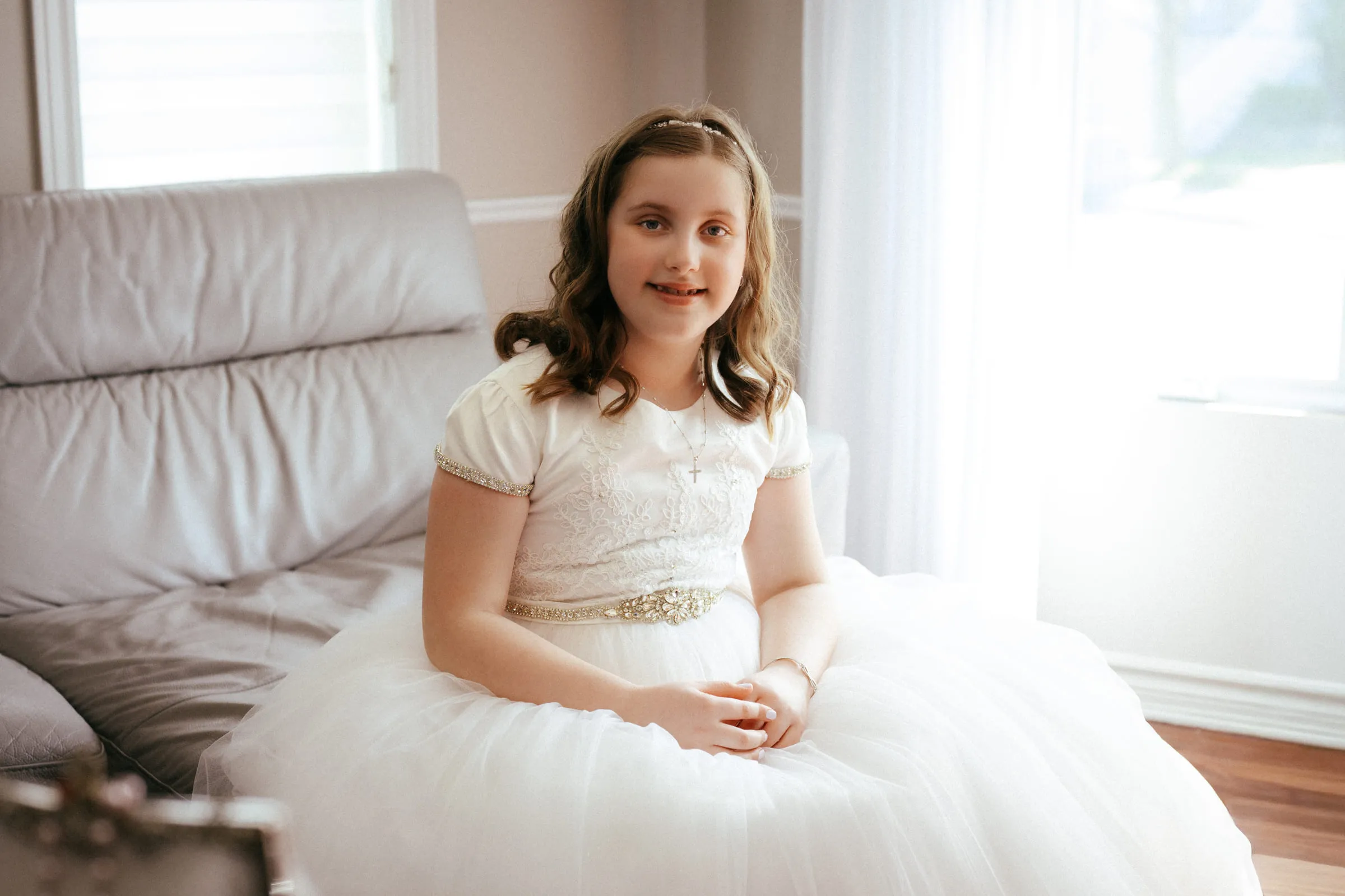 The girl seated in her communion dress beside a bright window