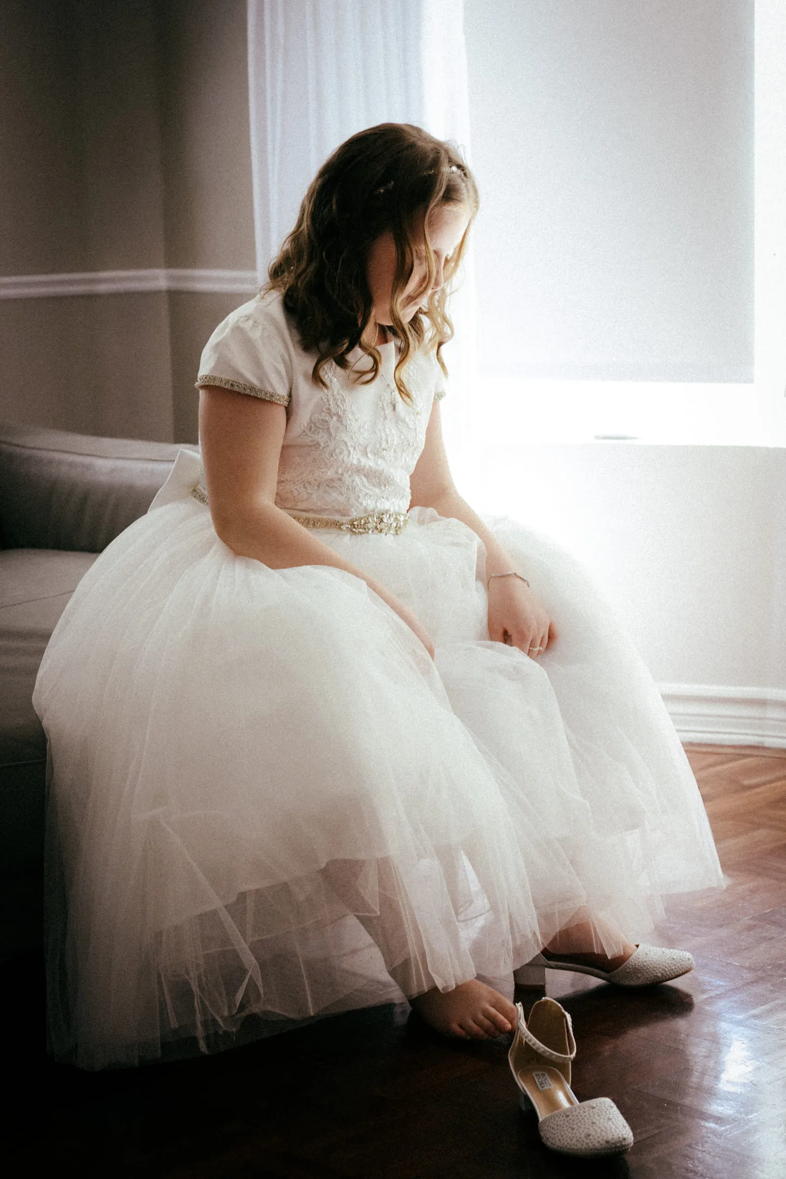 The girl leaning down to put on her shoes, her tulle skirt spread around her