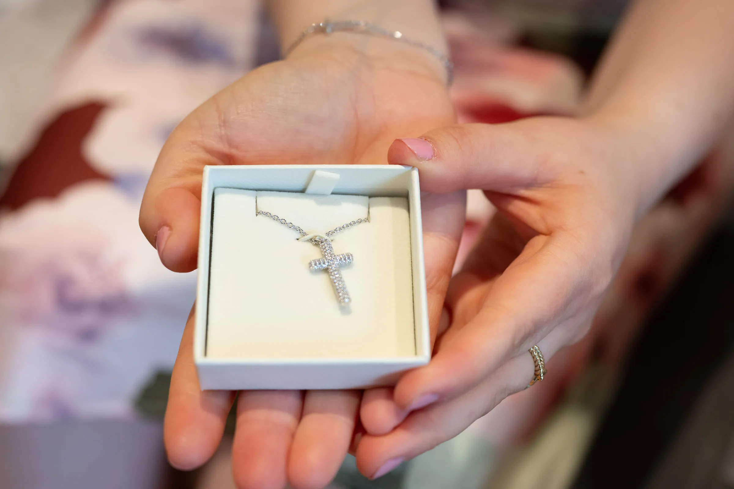 A diamond cross pendant in its box, held in cupped hands