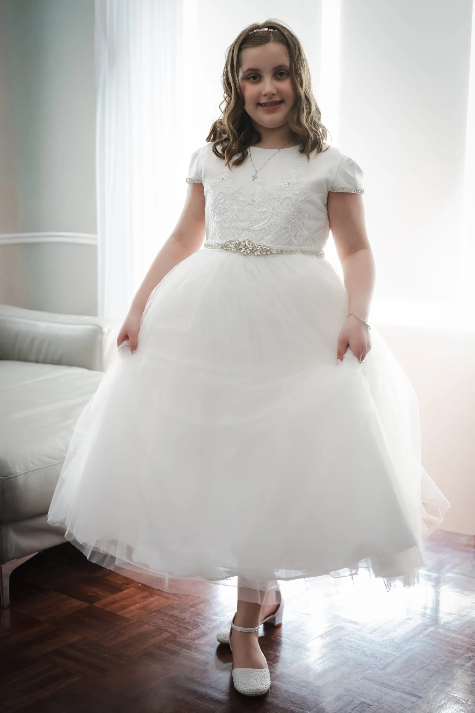 A girl standing in her full communion dress in the window light