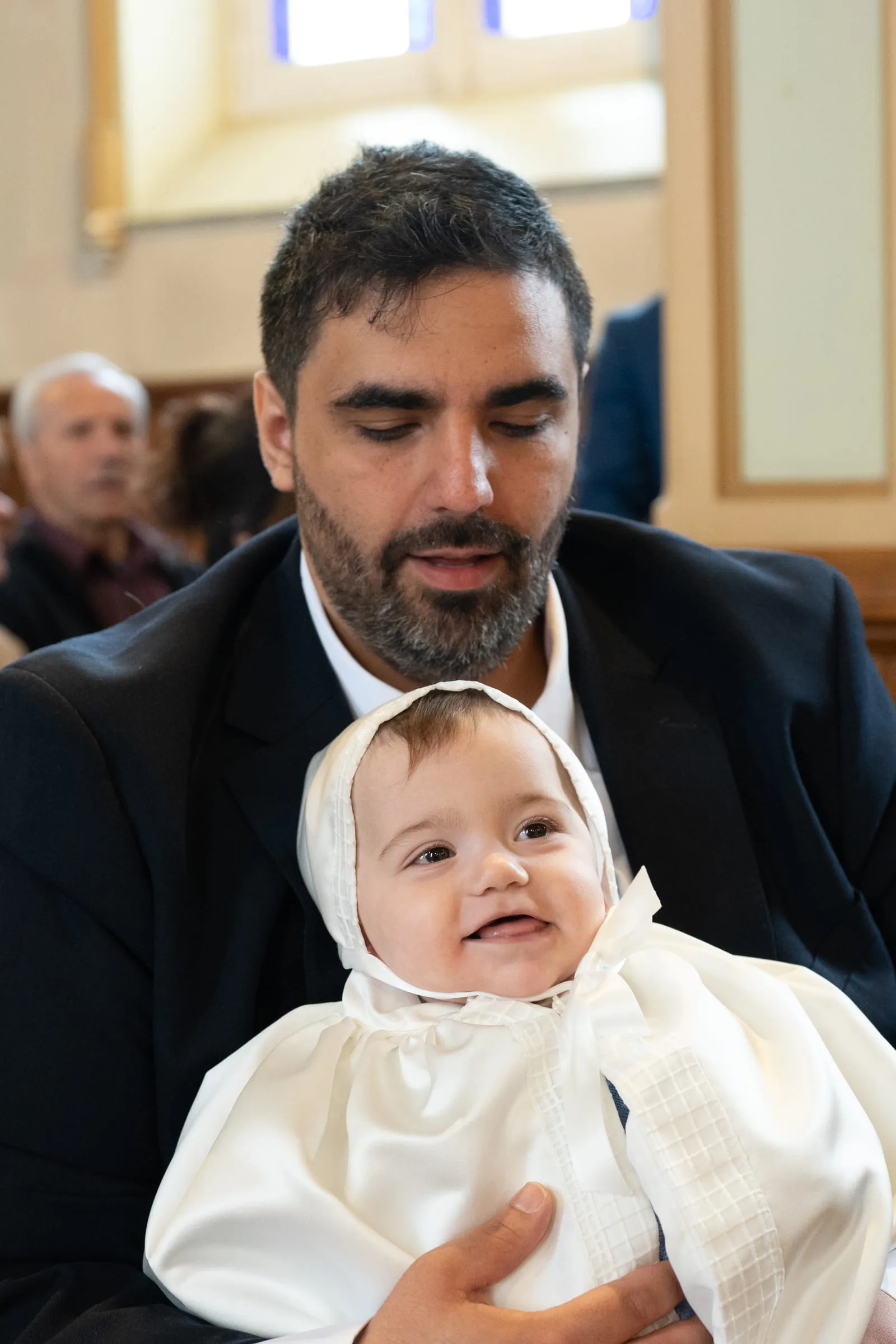 The baby’s father holding him in his christening gown and bonnet, the baby smiling