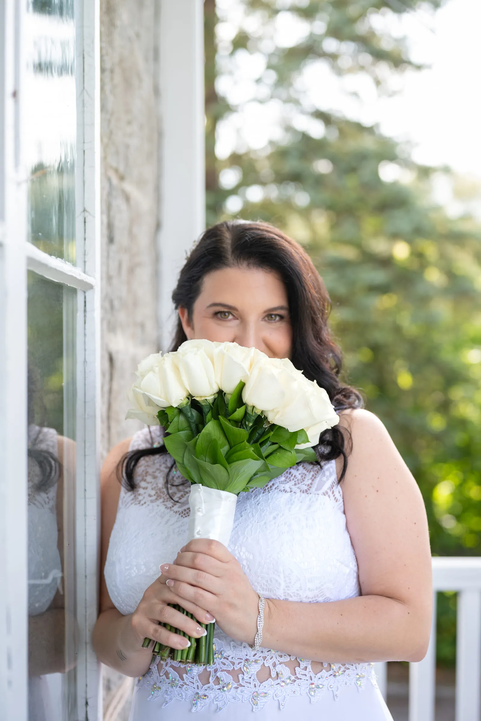 The bride holding her white rose bouquet up to her face in a sunlit doorway