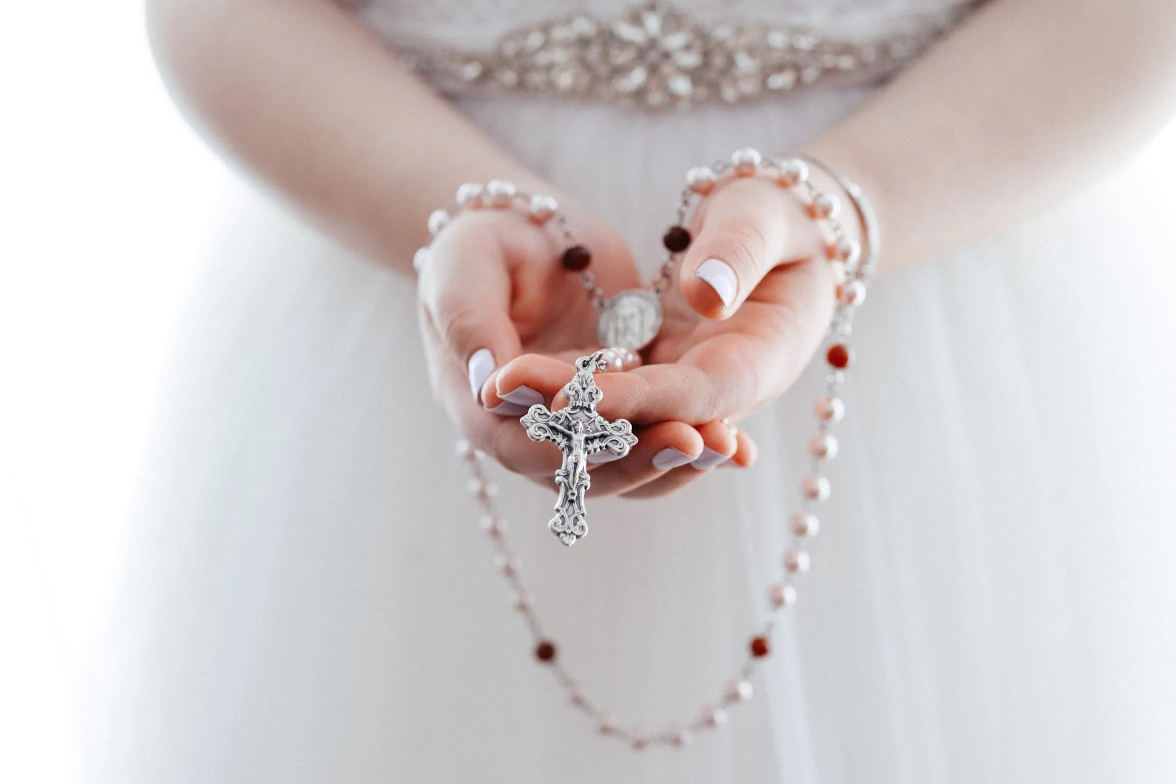 A rosary and crucifix held in the girl’s cupped hands against her white dress