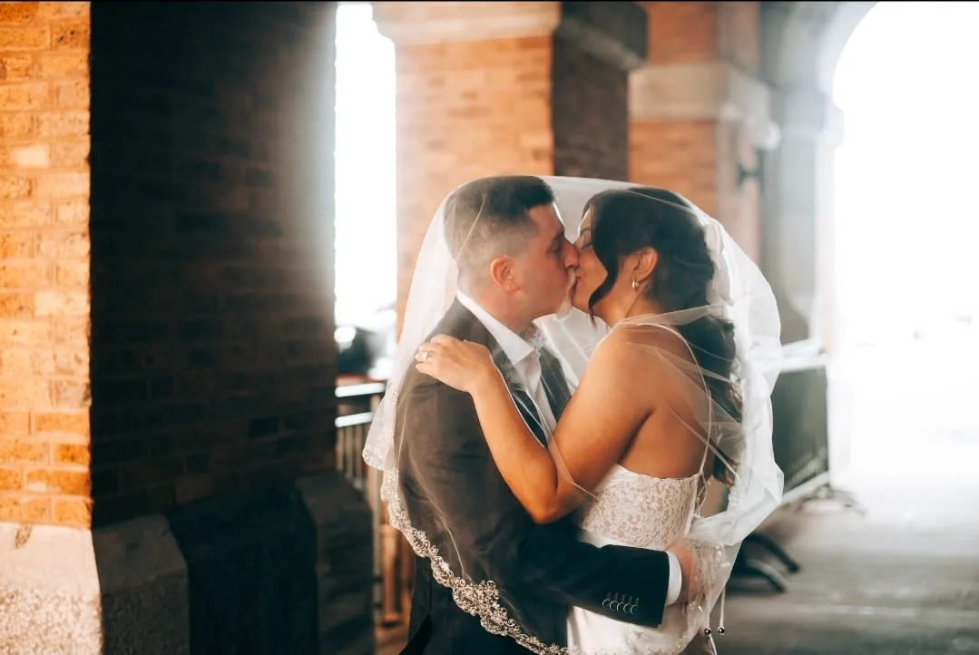 A bride and groom kissing under her veil in a warm brick archway