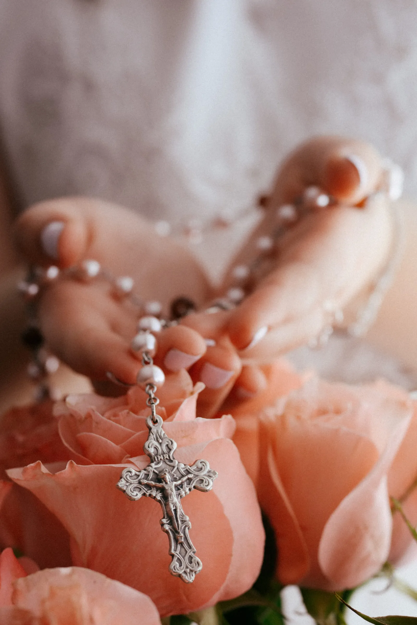 A silver crucifix and rosary resting on peach-coloured roses