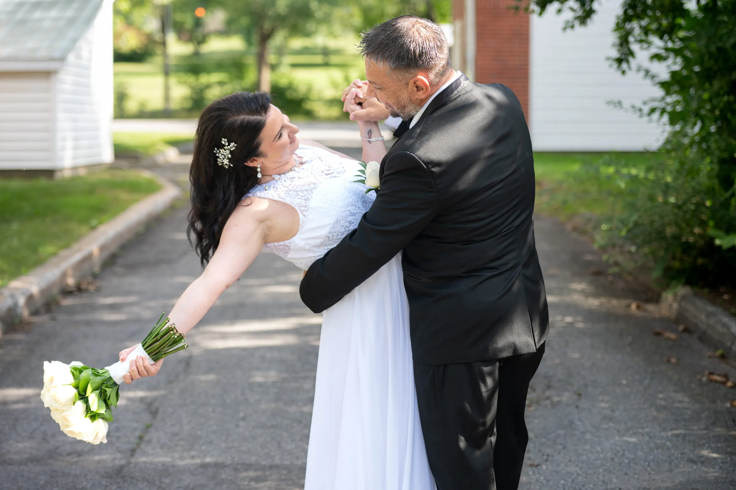 The groom dipping the bride and kissing her hand as she holds her bouquet out behind her