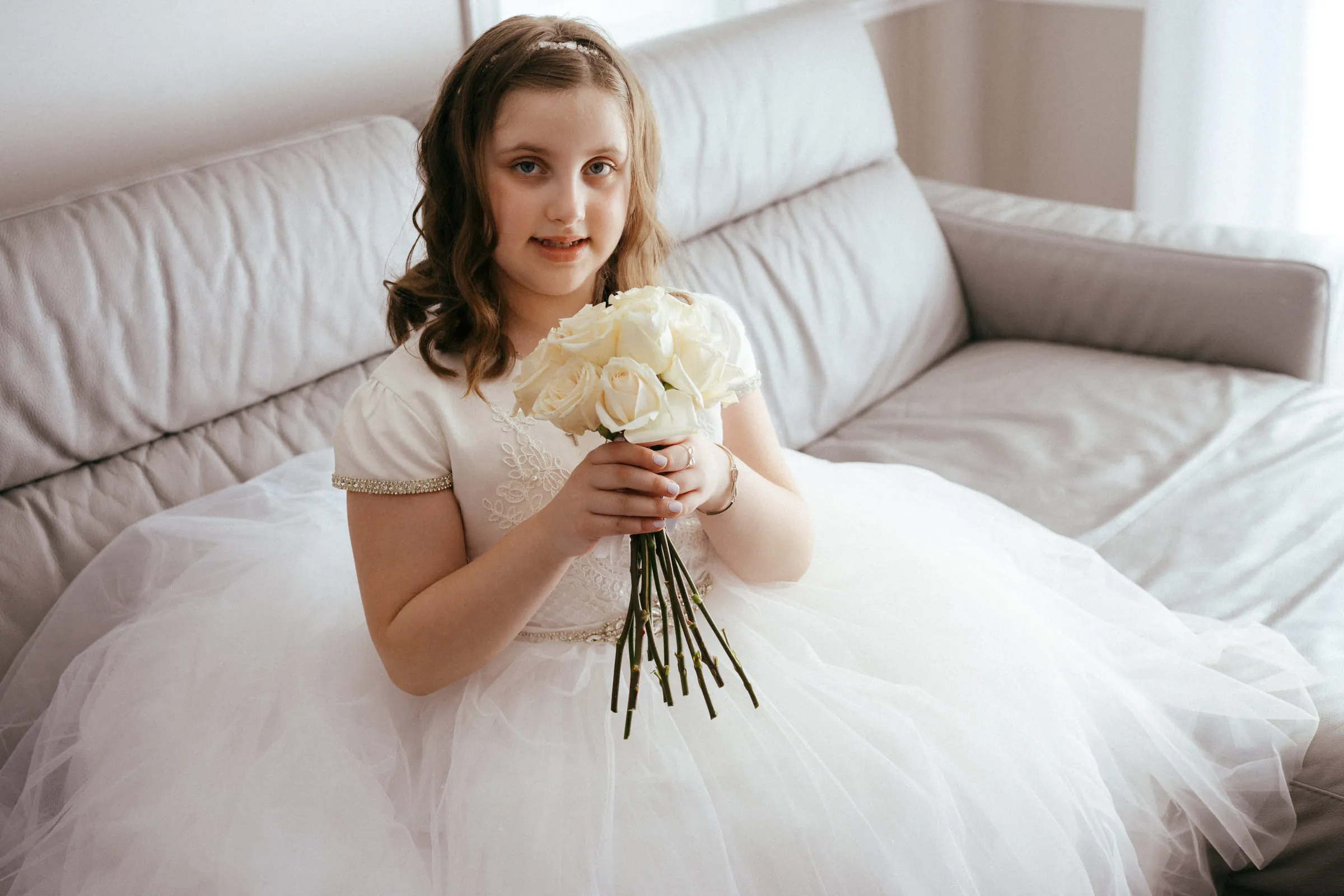 The girl seated holding a small bouquet of white roses