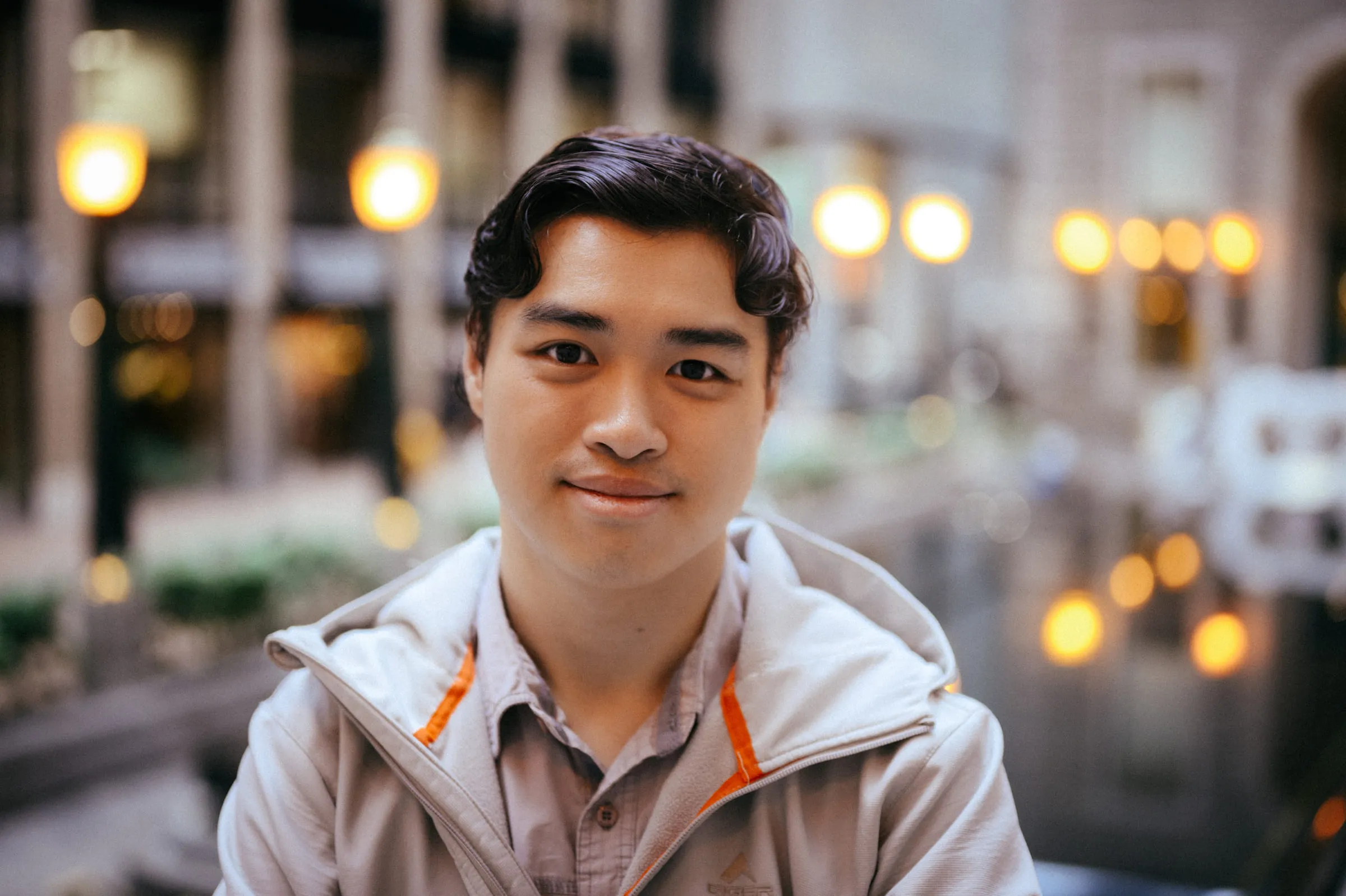 A young man smiling, warm street lights out of focus behind him
