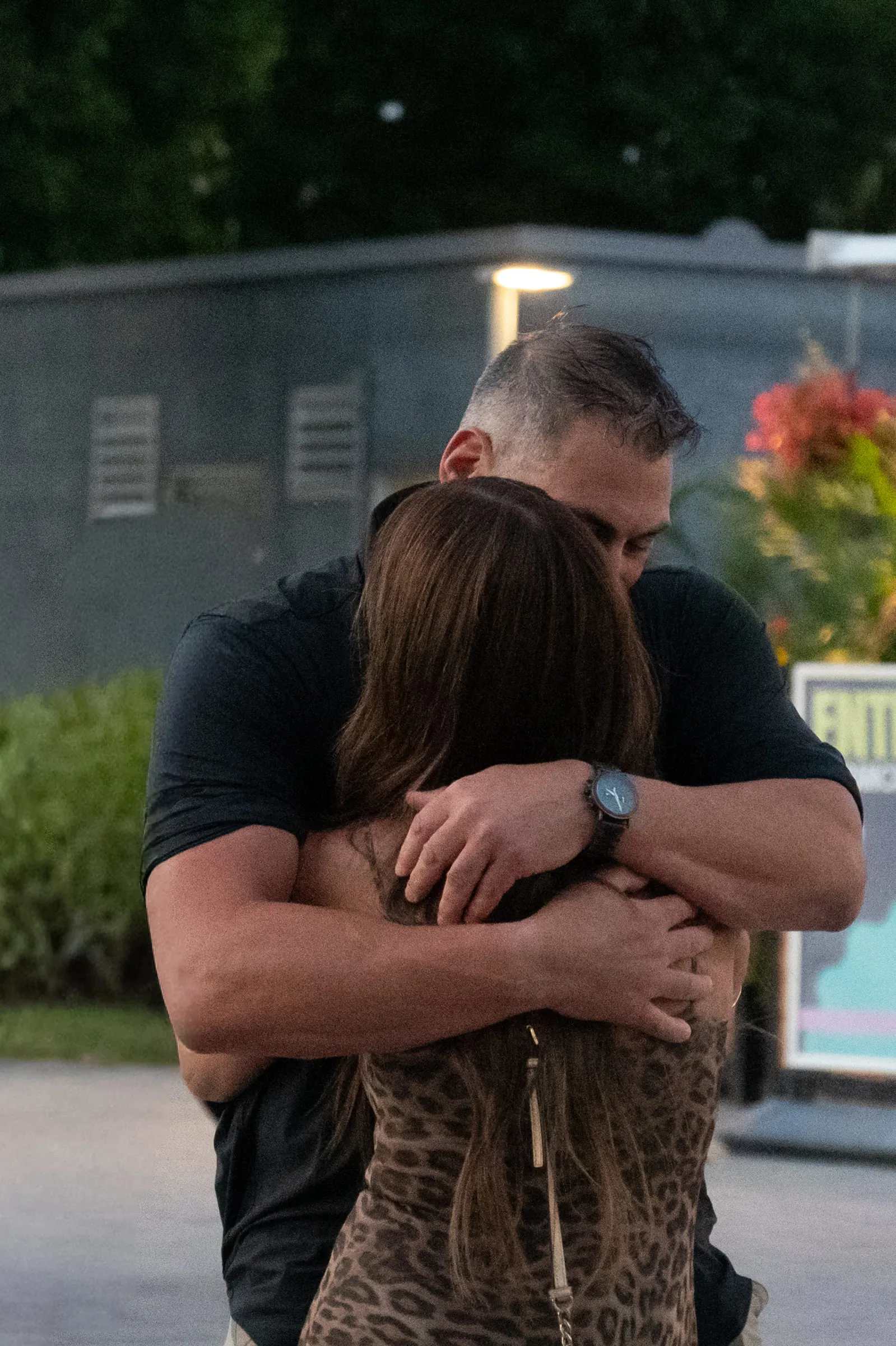 She holds on to him tightly, her face against his shoulder