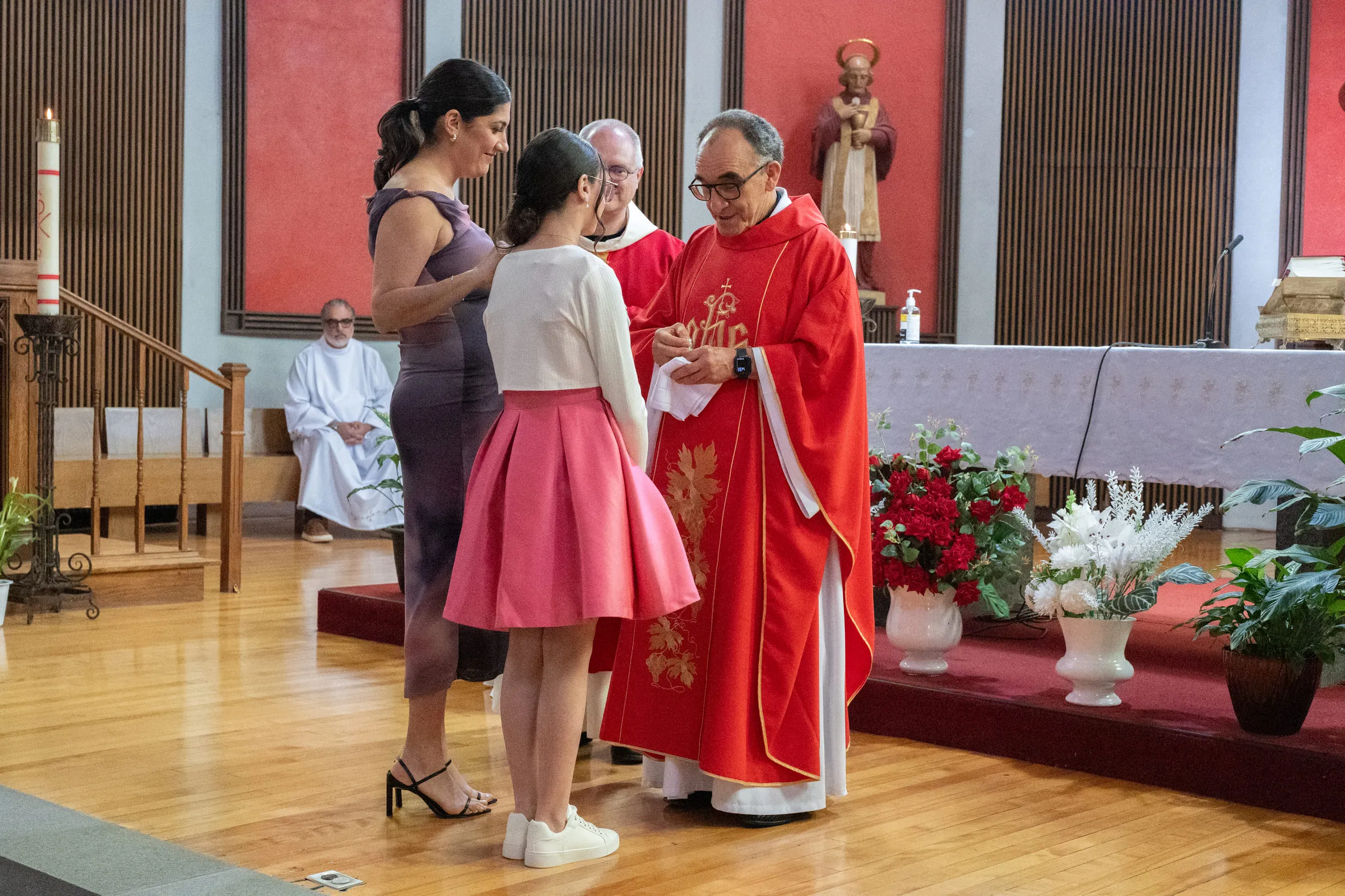 The girl standing before the priest in red vestments at the altar