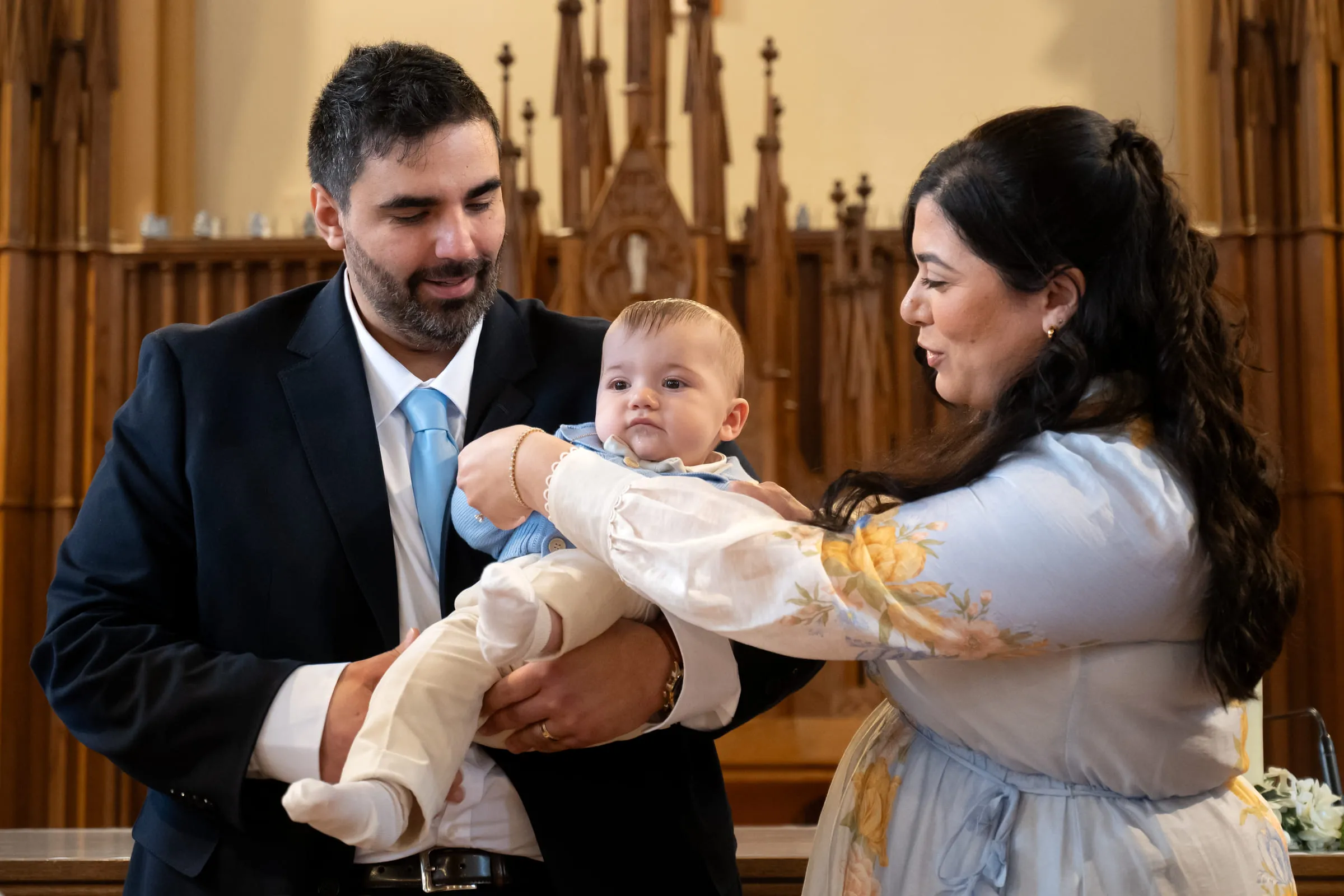 Both parents holding the baby between them in front of the altar