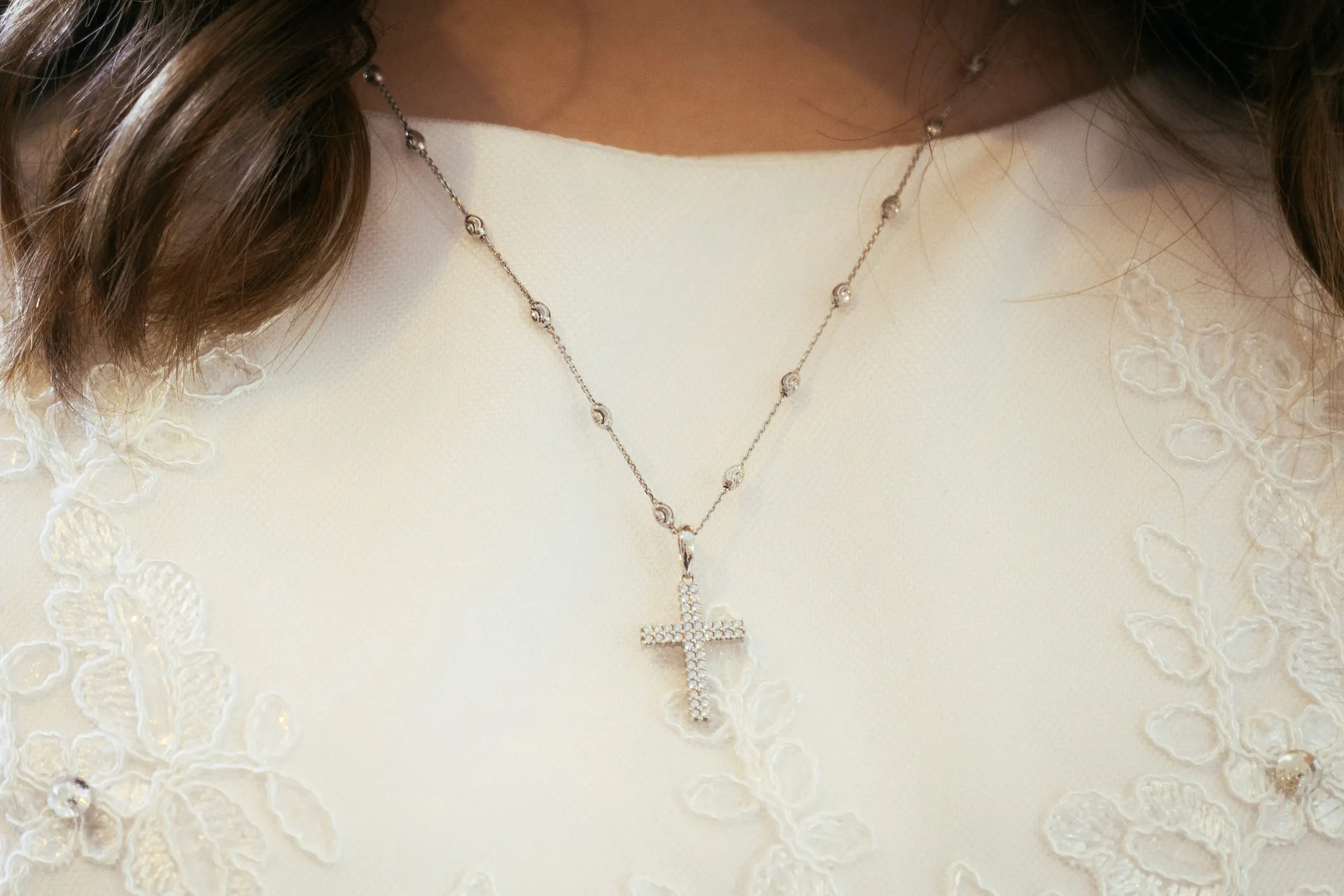 A small cross pendant resting against the lace of the communion dress