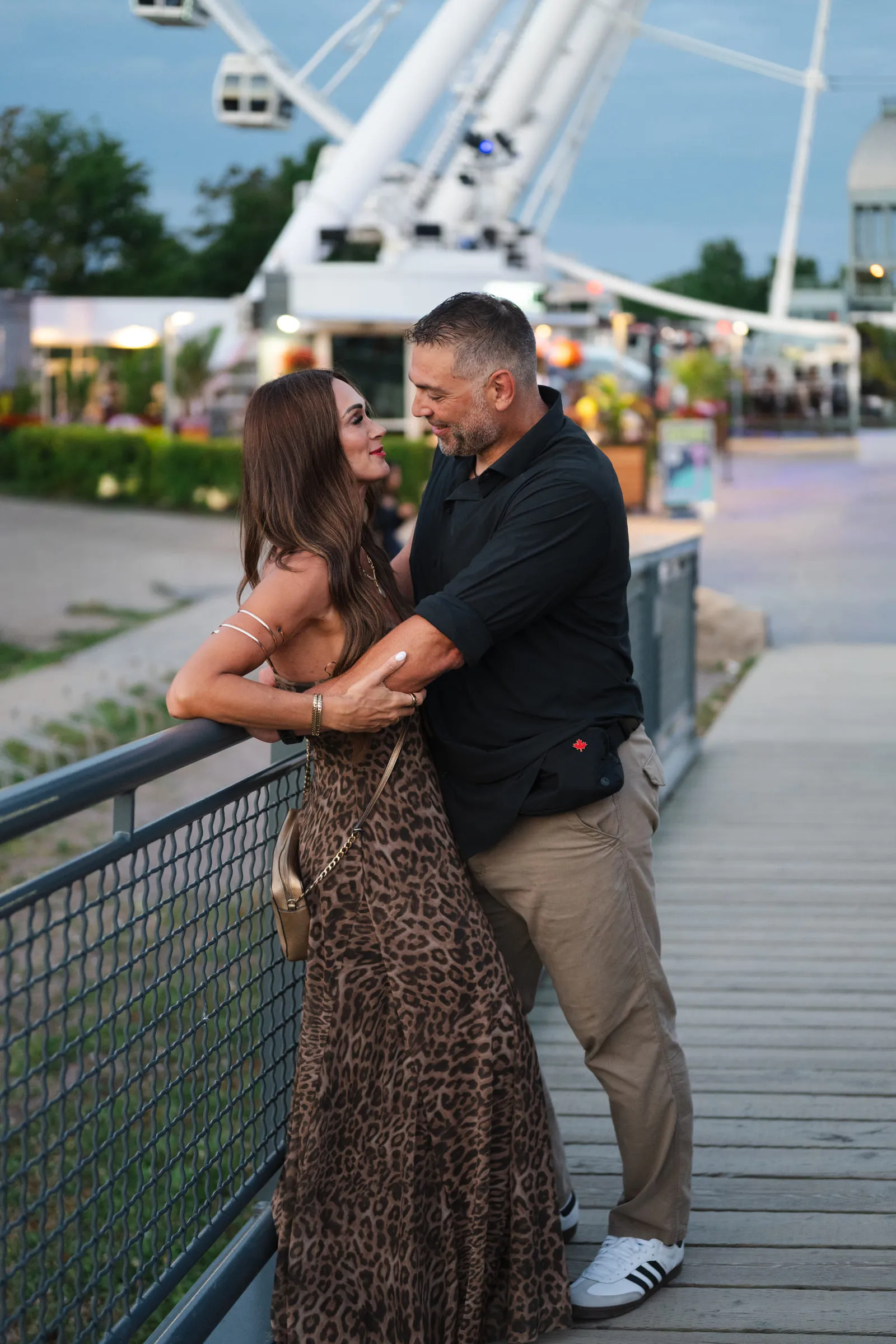 The couple holding each other on the boardwalk with the Ferris wheel behind them