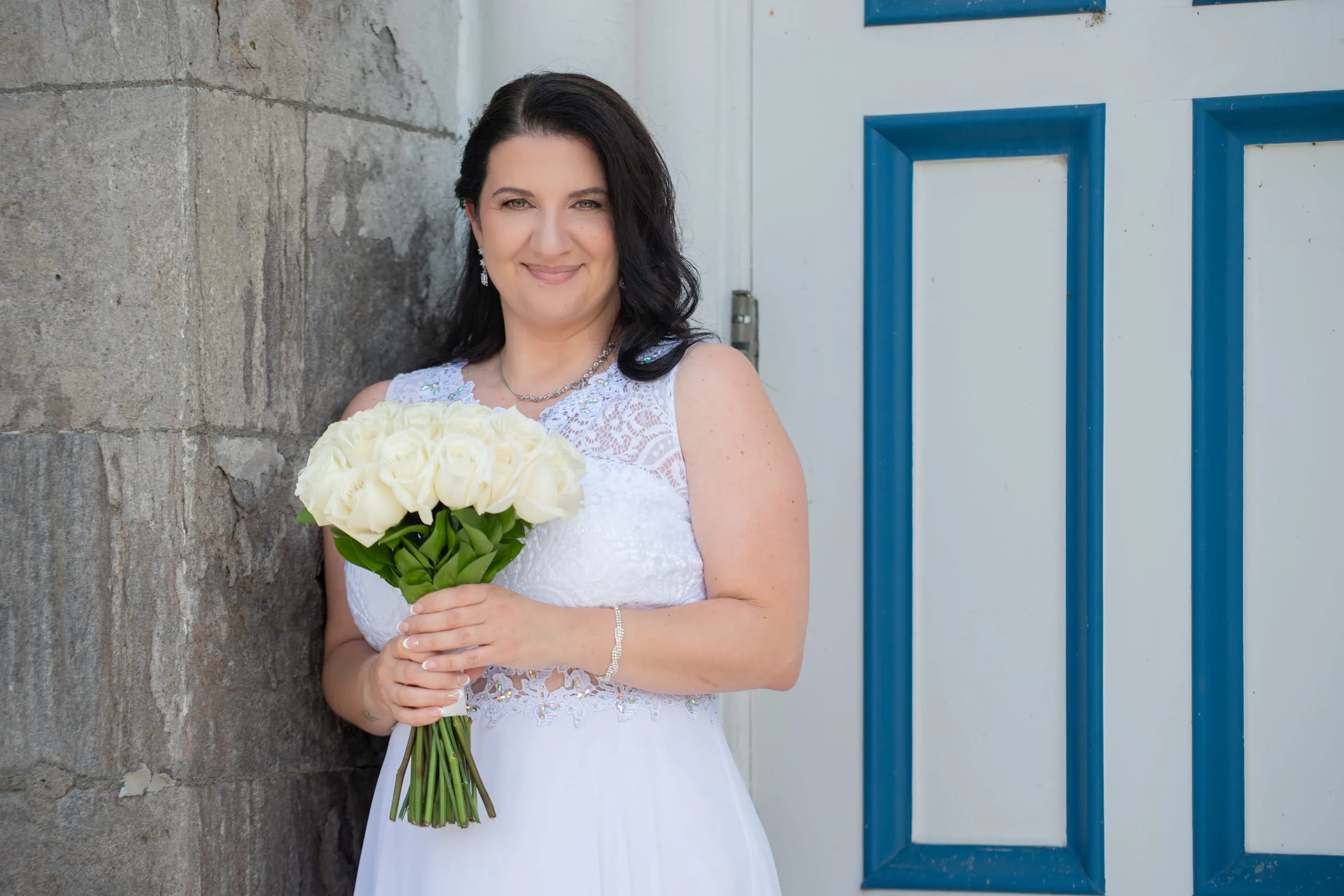 The bride with her bouquet against a stone wall beside a blue and white door