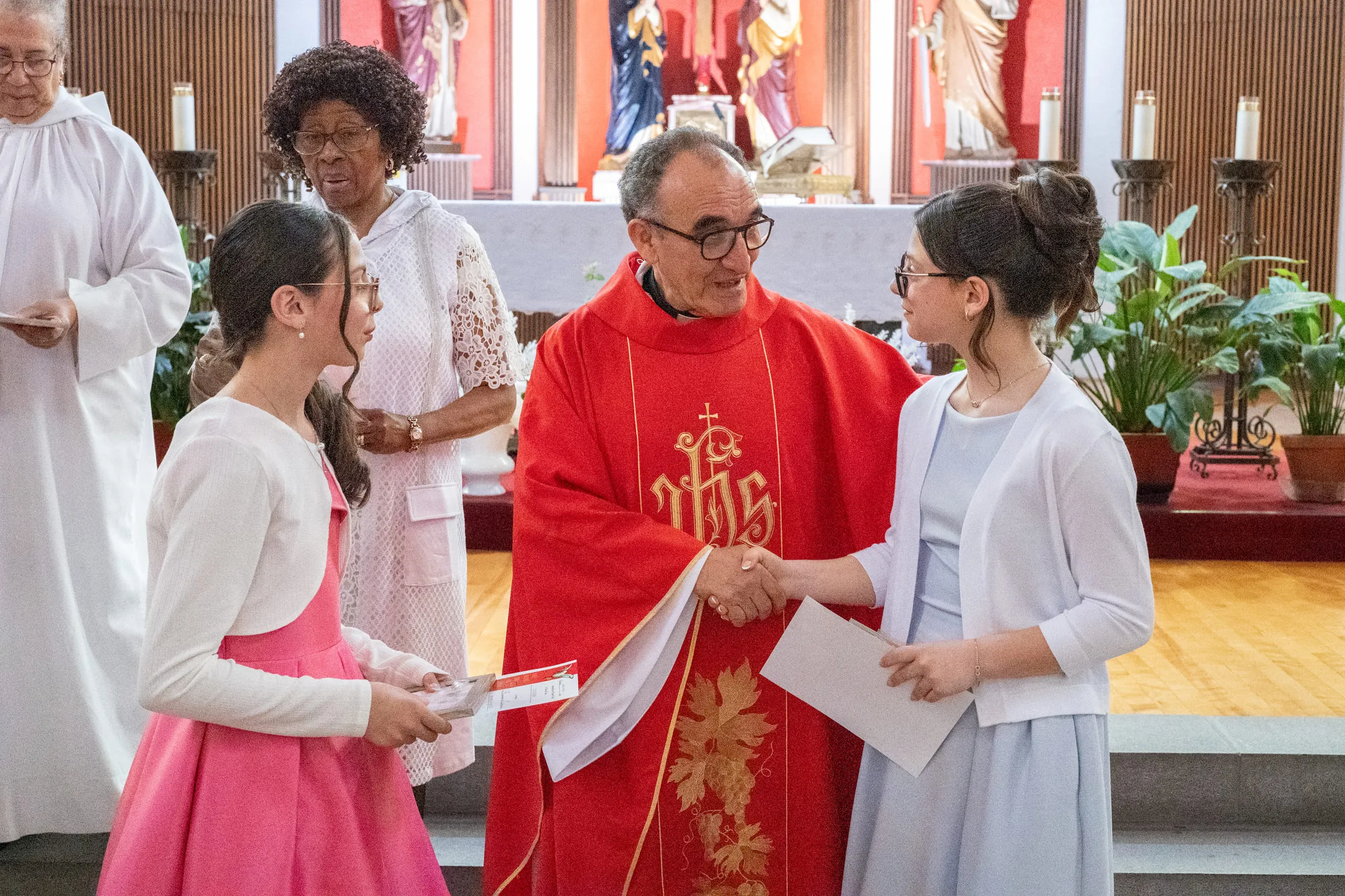 The priest handing confirmation certificates to two of the girls