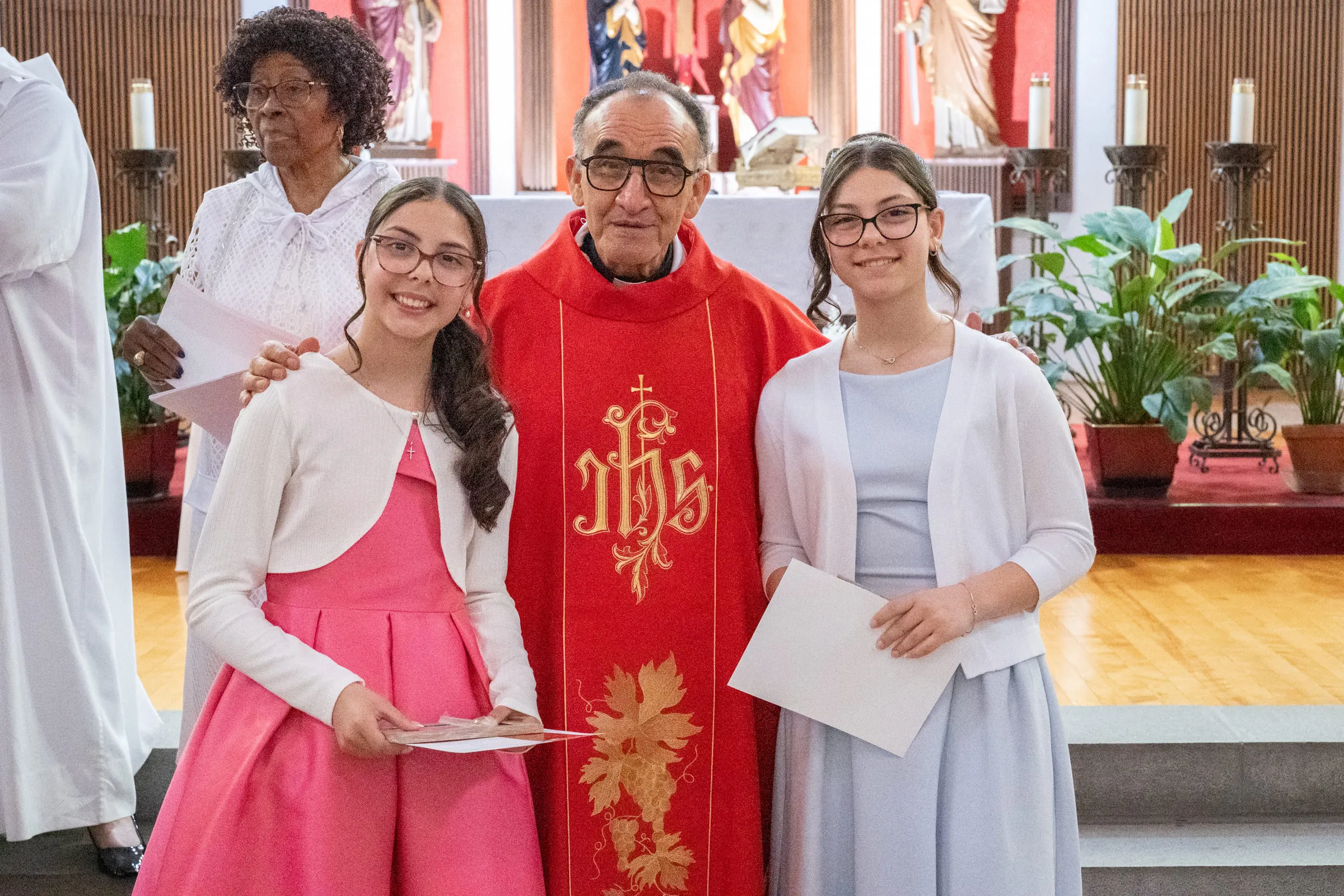 The two girls standing with the priest, certificates in hand