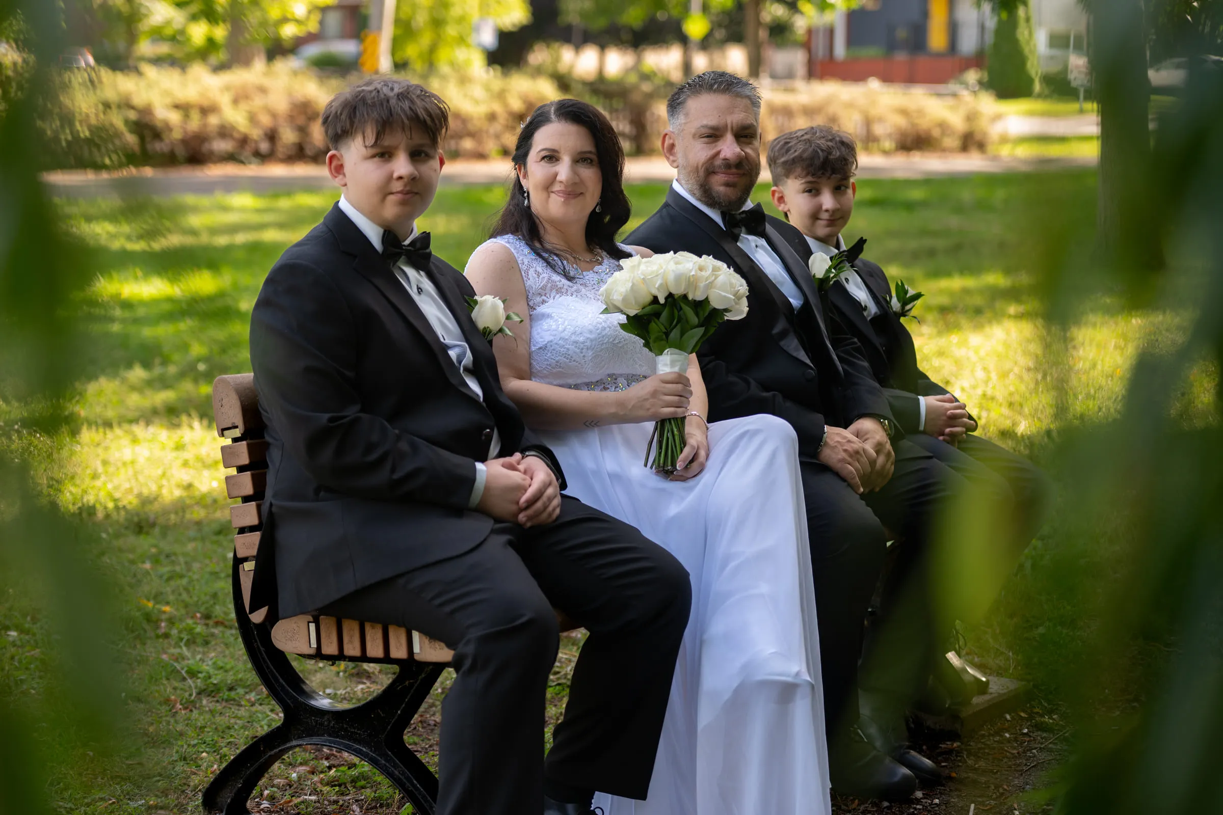 The couple and their two sons seated together on a park bench, framed by leaves