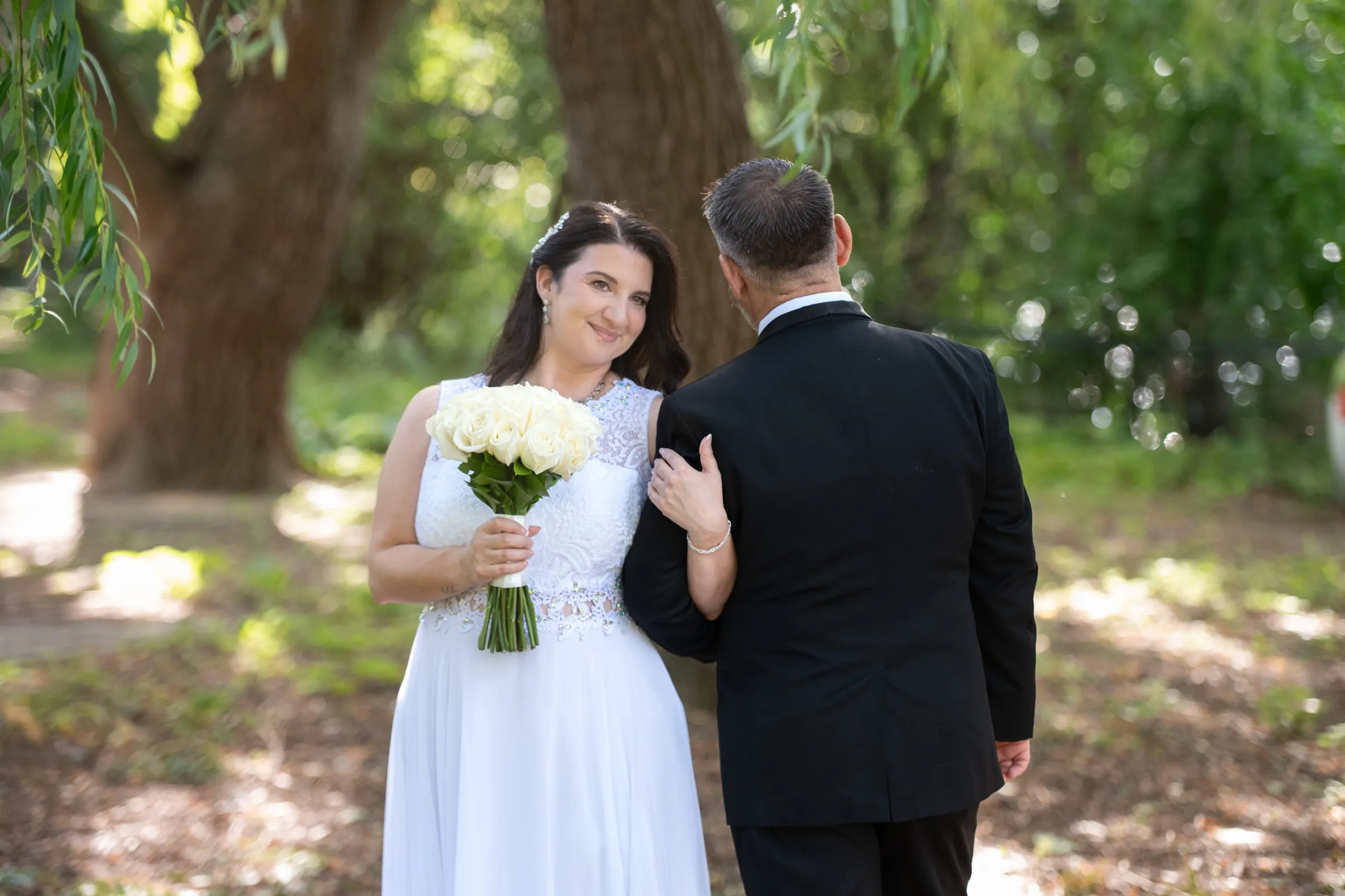 The bride resting a hand on the groom’s shoulder among the willow branches